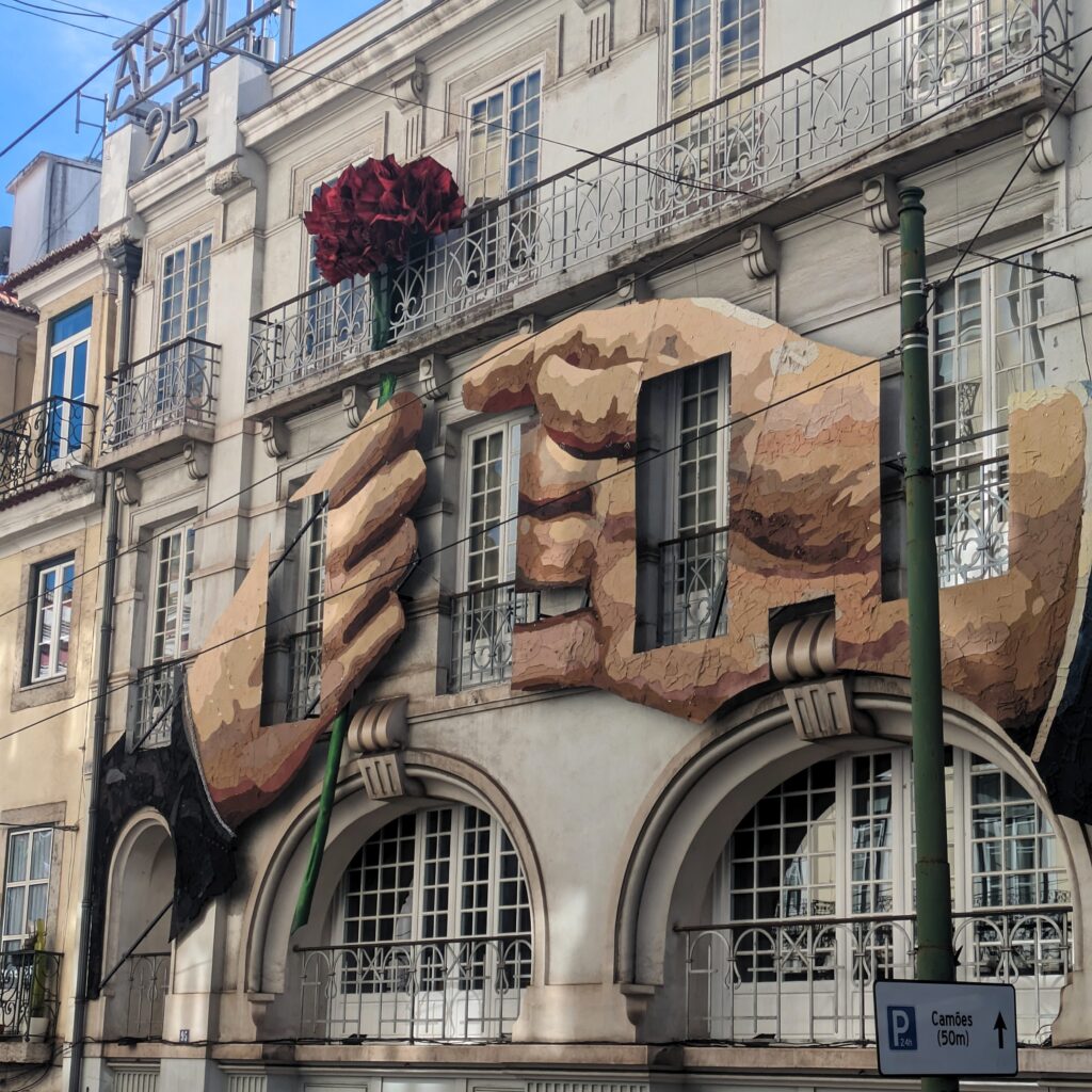 cravo_building_sqr Exterior of the Associação 25 De Abril building in Lisbon, with two large plaster hands on the side, one carrying a red carnation.