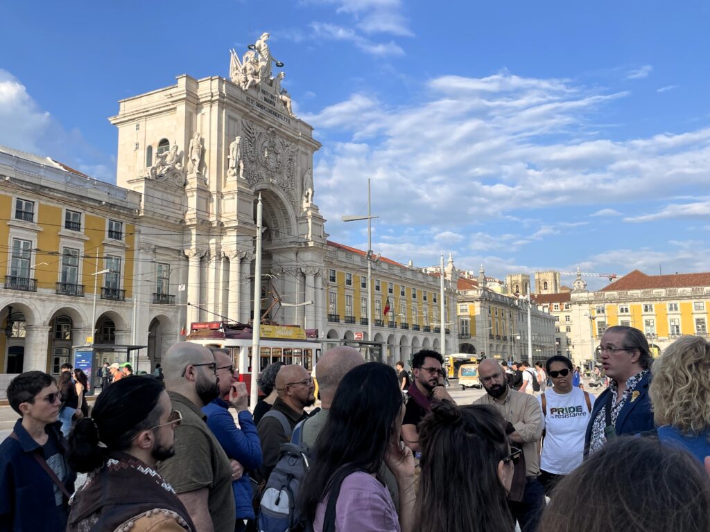 A group of people stand in a plaza featuring a large triumphal arch in downtown Lisbon.